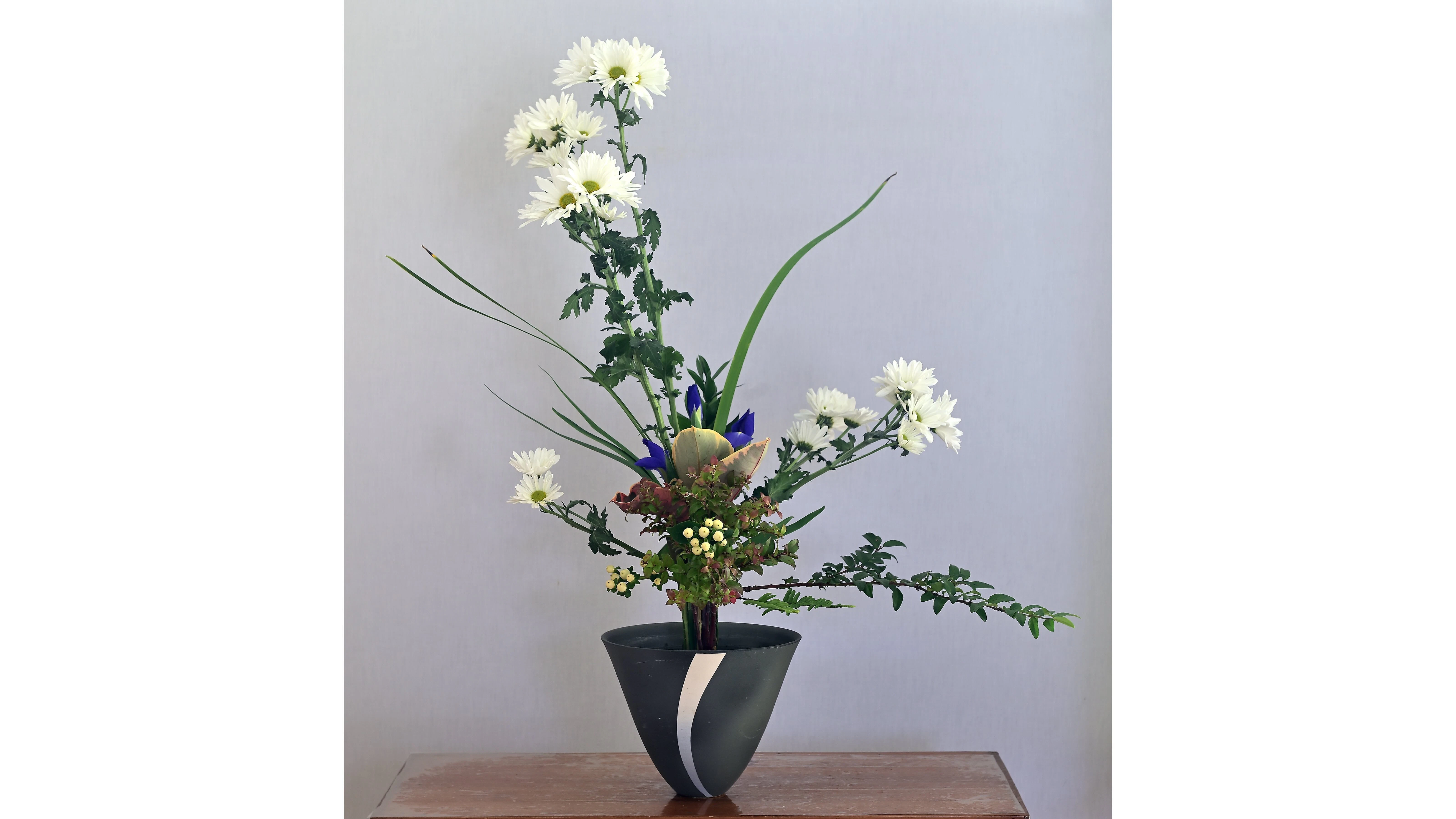 Tinius chose iris, ruskus, chrysanthemum, huckleberry, hypericum, sword fern, and iris and rubber tree leaves for this rikka arrangement.