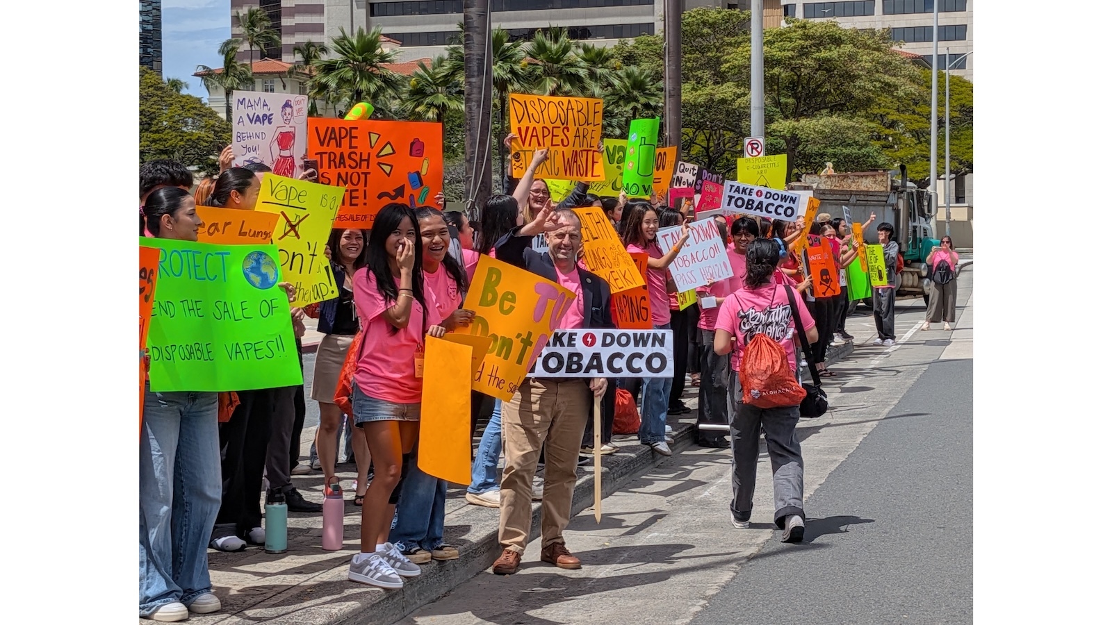 Gov. Josh Green waves signs with keiki outside the State Capitol.
