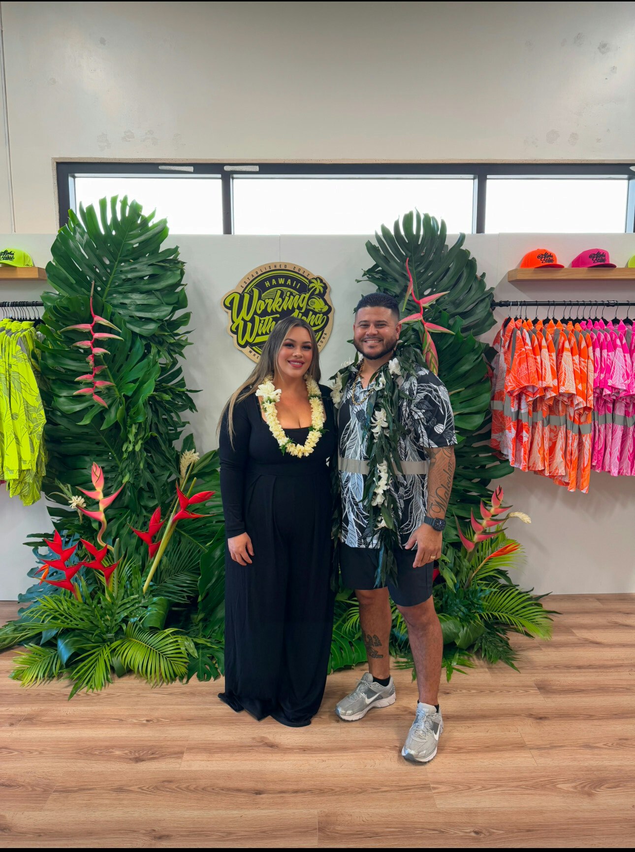 Corry and Shane Ahlo pictured at their studio with bright shirts in the back.