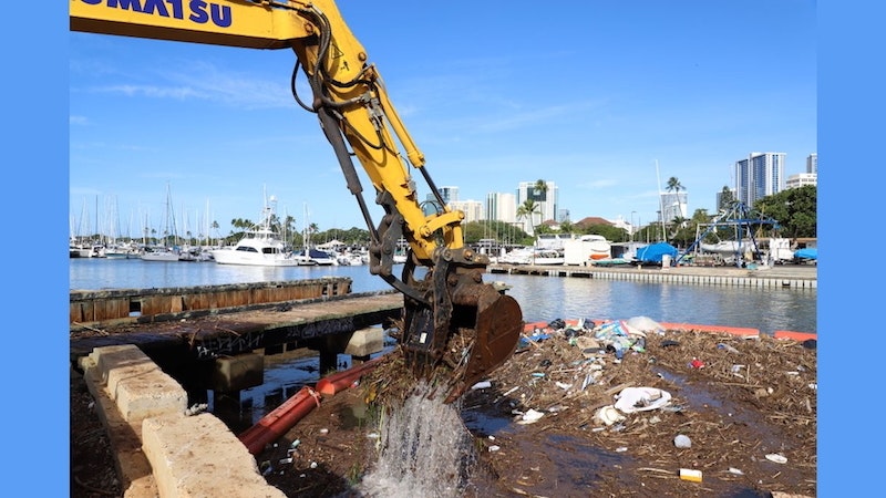 Trash being picked up by a crane in a boat harbor.