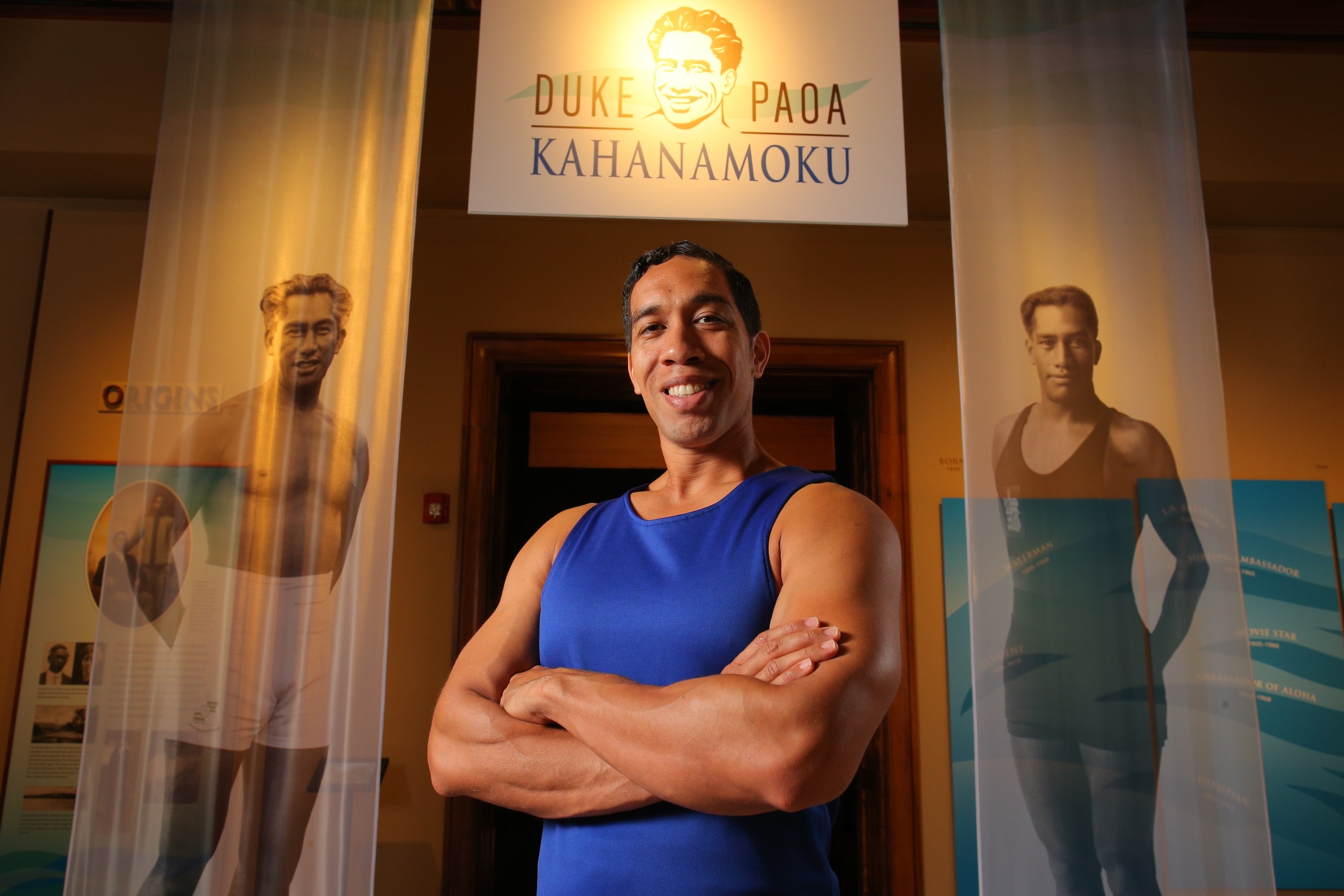 Actor Moses Goods stands beside photos of Duke Paoa Kahanamoku.