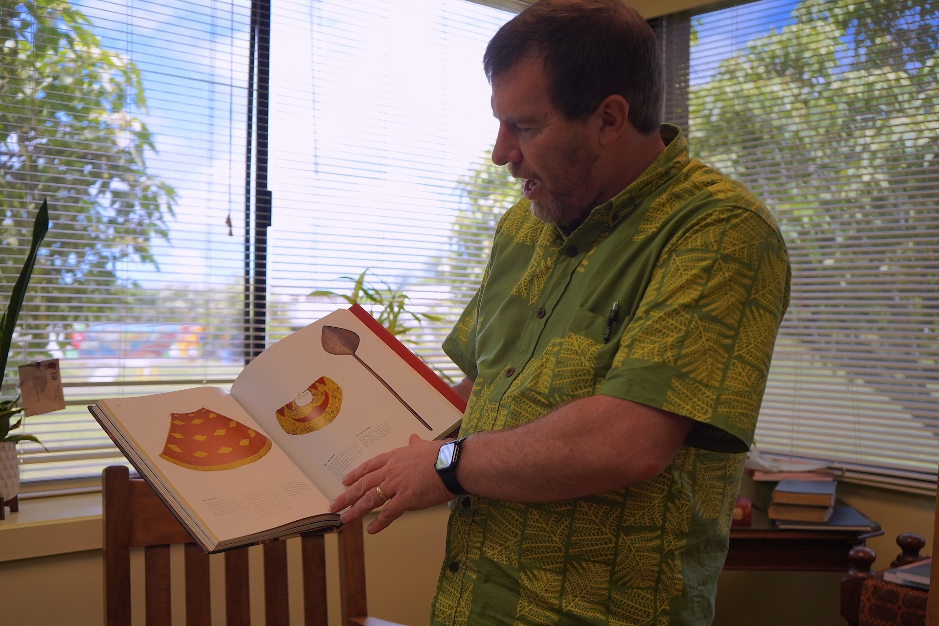 Helgen pictured holding one of the books in his office. Photo by Kelsey Kukaua Medeiros