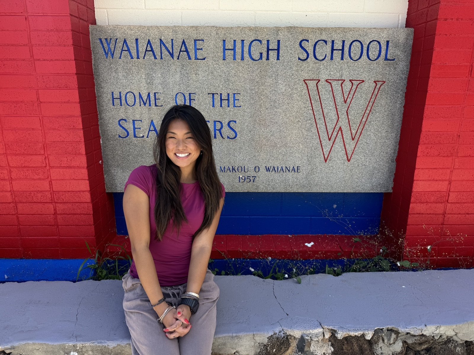 Emily Burt, a high school biology teacher, is in her second Teach for America corps year. Pictured here, she sits in front of the Waiʻanae High School sign.