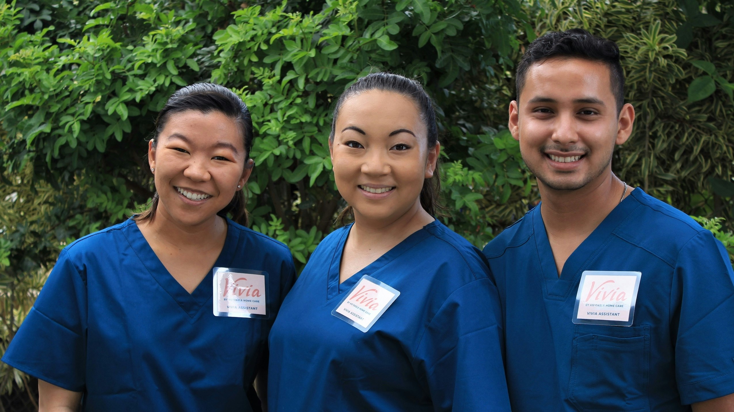 Three caregivers dressed in blue scrubs smiling.