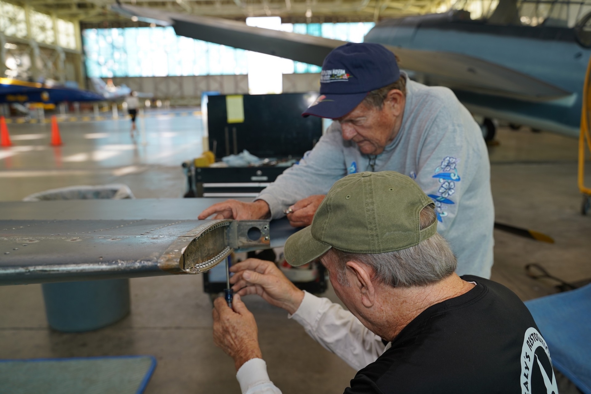 Montgomery (wearing blue cap) and Mark Erwin disassemble a stabilizer on the tail section of an SBD-5 Dauntless, a World War II-era dive bomber. Credit: PHAM.
