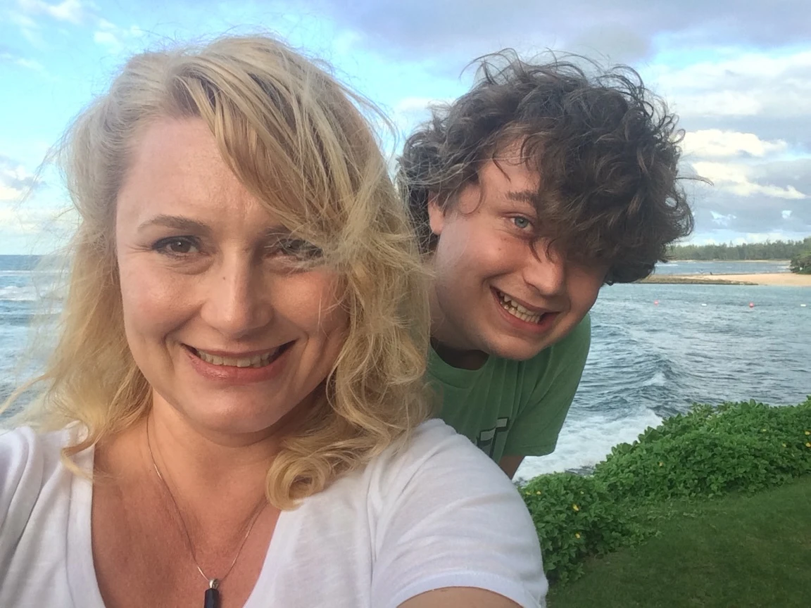 Mom and son smile with beach in background.