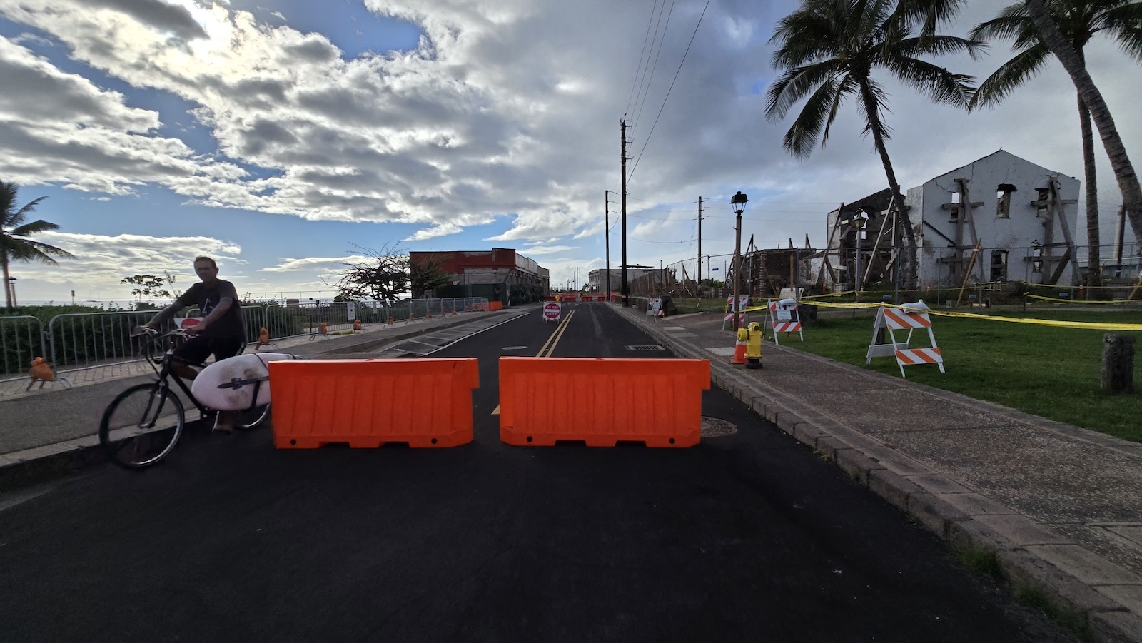 A man rides a bicycle past barricades on Front Street in Lahaina.
