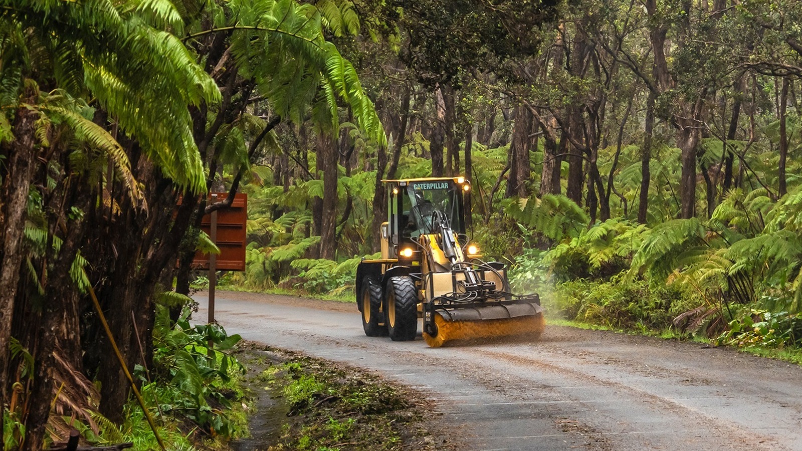 A National Park Service heavy equipment operator sweeps Crater Rim Drive East after scraping fallen trees and branches earlier.