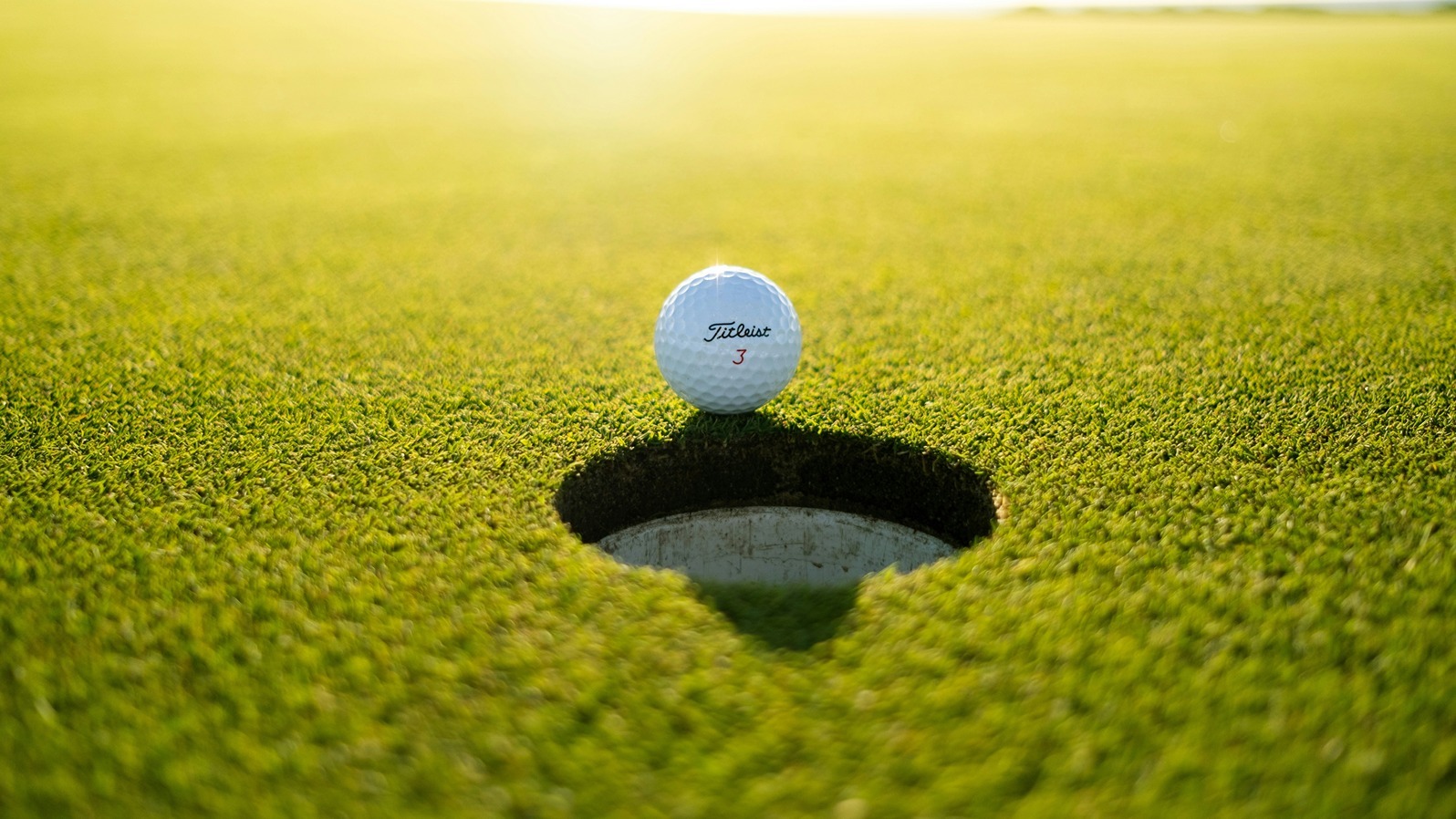 A golf ball is perched on the edge of the hole.