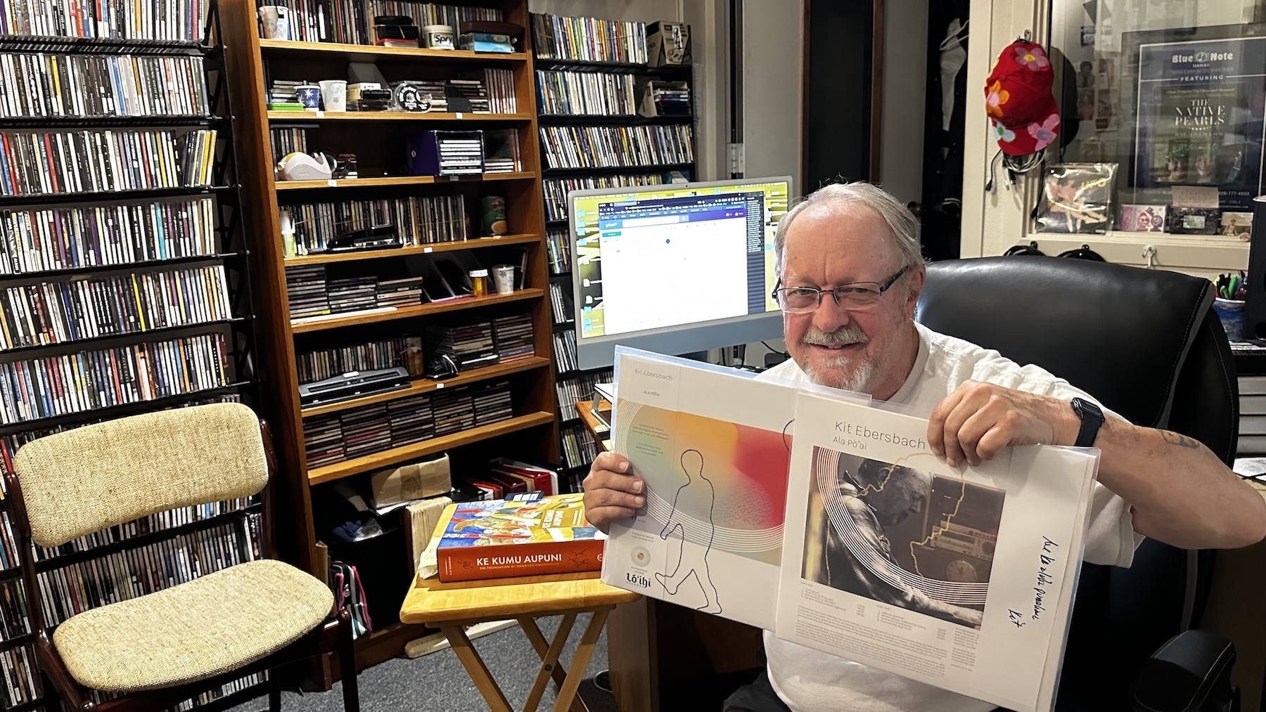 Kit Ebersbach holds his new album, “Ala Pōʻai,” at Pacific Music Productions recording studio in Chinatown. Behind him are CDs, which he uses to curate in-flight programming for Hawaiian Airlines.