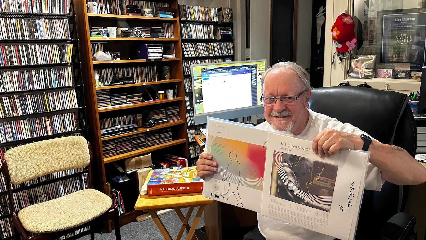 Kit Ebersbach holds his new album, “Ala Pōʻai,” at Pacific Music Productions recording studio in Chinatown. Behind him are CDs, which he uses to curate in-flight programming for Hawaiian Airlines.