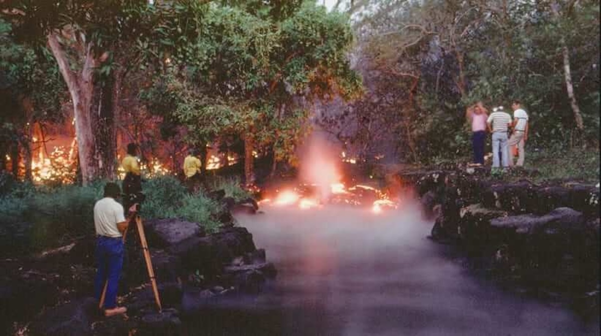 On March 31, 1987, the ongoing eruption of Kīlauea destroyed the beloved wahi pana known as "Queen’s Bath" a freshwater pool supplied by a natural spring that formed within by a collapsed lava tube. Pictured: Onlookers watch helplessly as Queen's Bath is filled in by molten lava. - Courtesy Photo