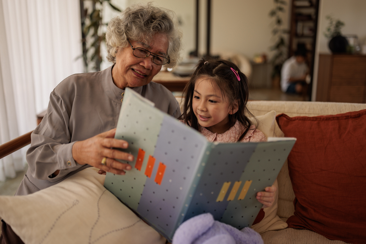 Multi-generation family, cute girl reading stories from a book with her grandmother at home.