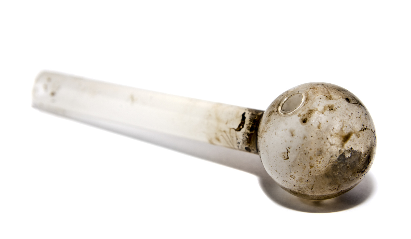 View of a glass pipe used to smoke illegal drugs.  This particular pipe was confiscated by police and was used to smoke methamphetamine.  Image shot at the police station.  Focus on round end with natural shadow.
