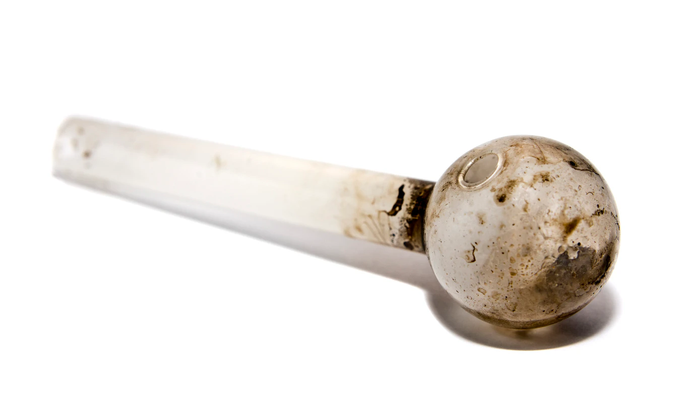 View of a glass pipe used to smoke illegal drugs. This particular pipe was confiscated by police and was used to smoke methamphetamine. Image shot at the police station. Focus on round end with natural shadow.